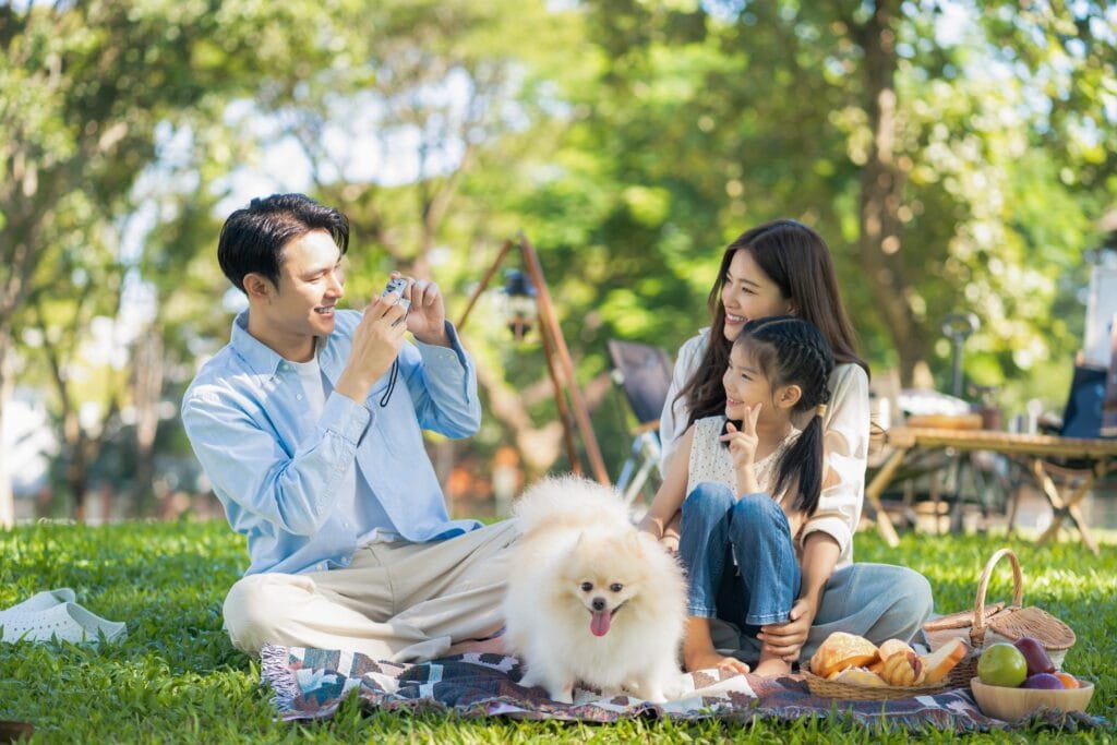 a family on a picnic with dad taking picture of mom and daughter